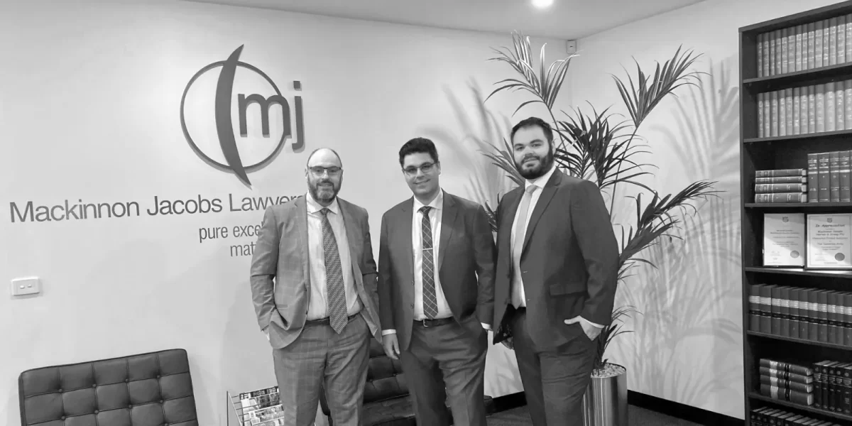 Three business partners standing together in from of a MJ Lawyers logo.