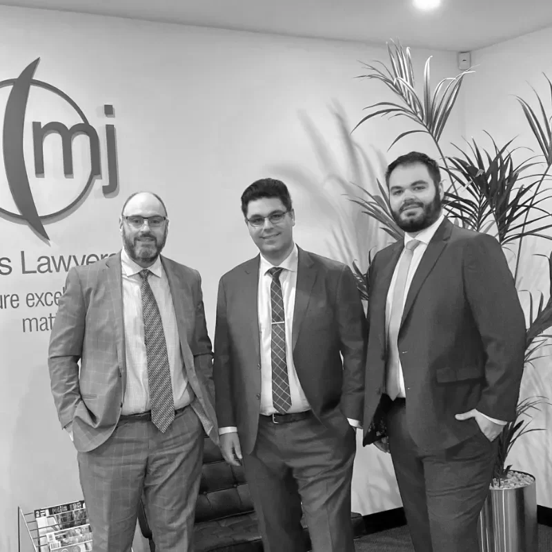 Three business partners standing together in from of a MJ Lawyers logo.